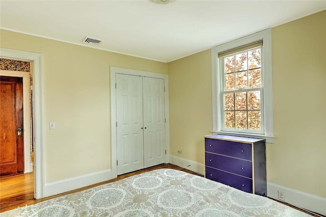 bedroom with baseboards, a closet, wood finished floors, and ornamental molding