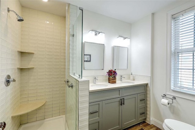 full bathroom featuring toilet, tiled shower, double vanity, and wood finished floors