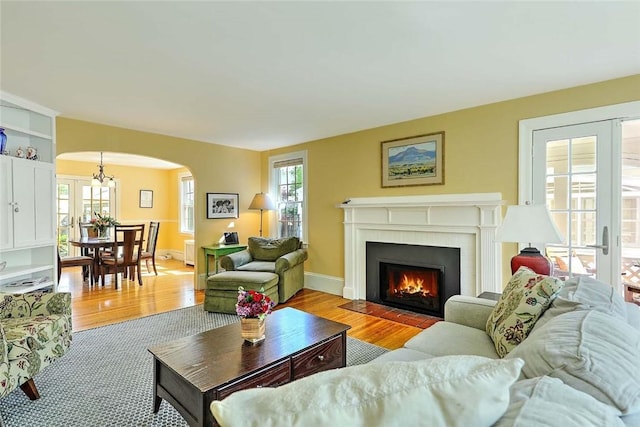living room with arched walkways, light wood-style floors, a fireplace with flush hearth, baseboards, and a chandelier