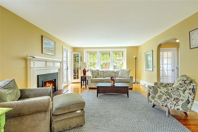 living area with light wood-style floors, arched walkways, a warm lit fireplace, and baseboards