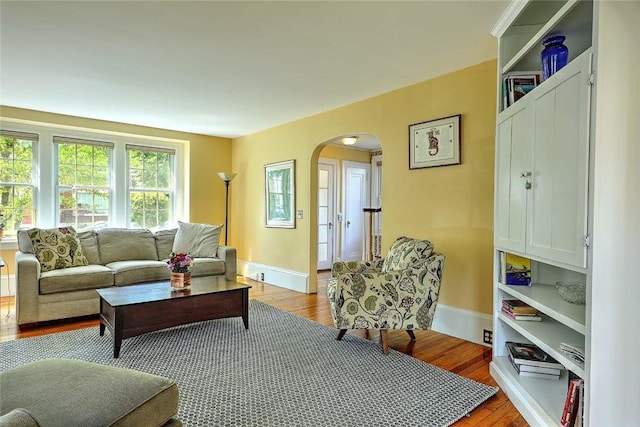 living room featuring arched walkways, light wood finished floors, and baseboards