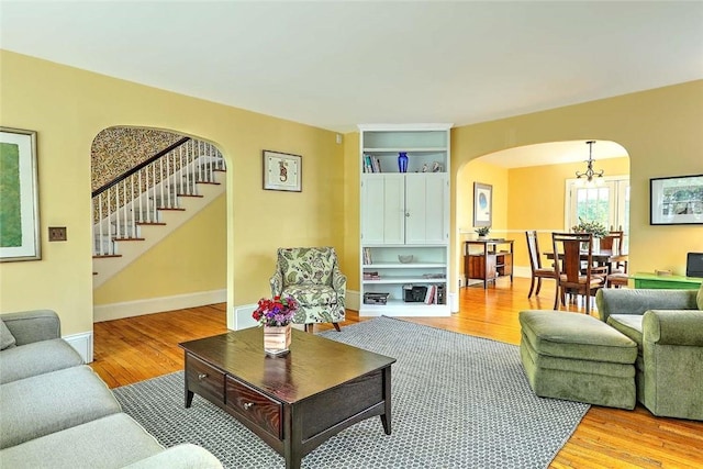 living area with arched walkways, light wood-style flooring, stairs, and a chandelier
