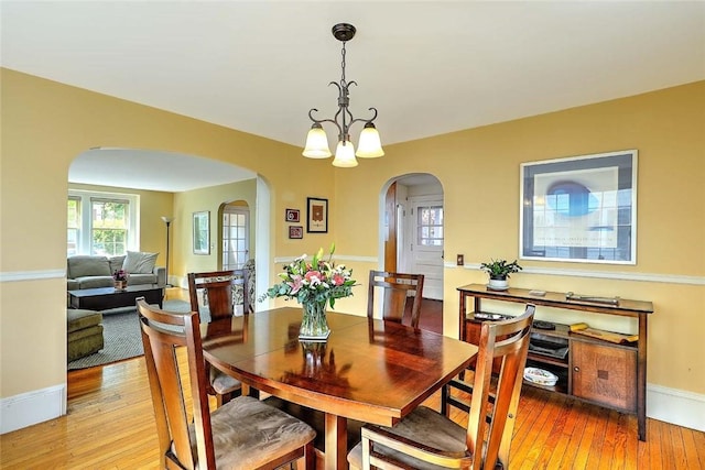 dining room featuring arched walkways, light wood-style flooring, baseboards, and a chandelier