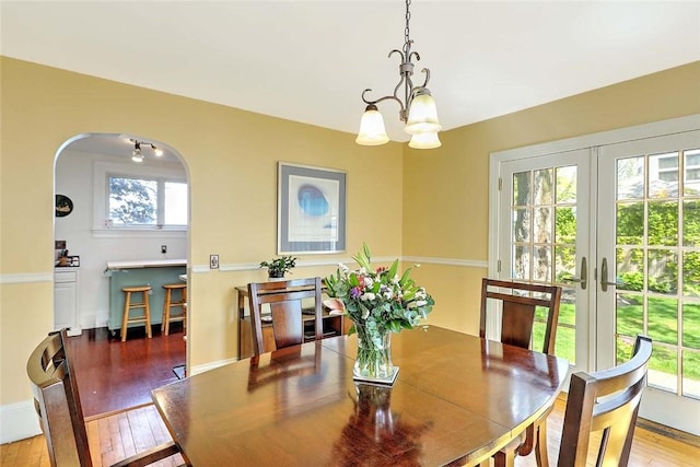 dining area featuring a chandelier, wood-type flooring, french doors, and arched walkways