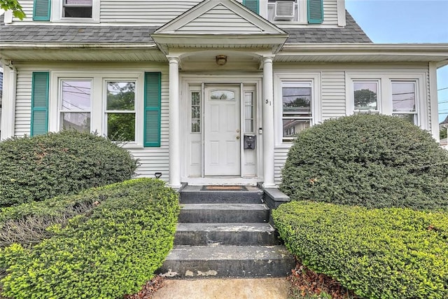 view of exterior entry with roof with shingles