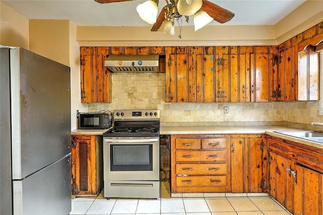 kitchen featuring appliances with stainless steel finishes, wall chimney range hood, ceiling fan, backsplash, and a sink