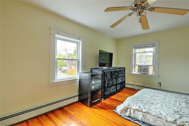 bedroom featuring a baseboard heating unit, multiple windows, and wood finished floors