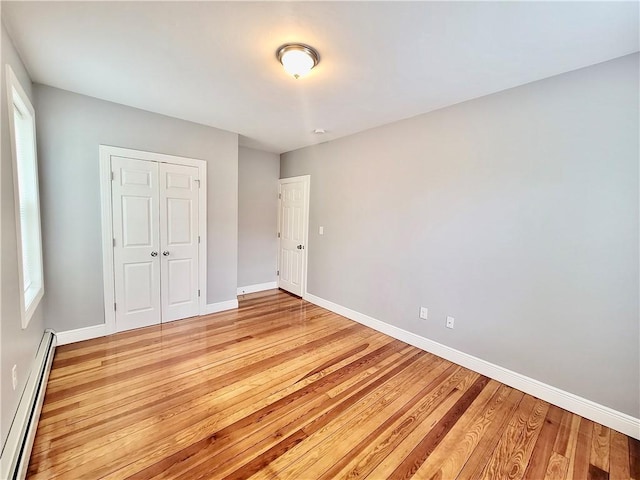 unfurnished bedroom with a baseboard heating unit, light wood finished floors, and baseboards