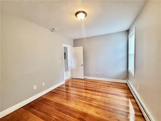 unfurnished room featuring a baseboard heating unit, hardwood / wood-style flooring, and baseboards