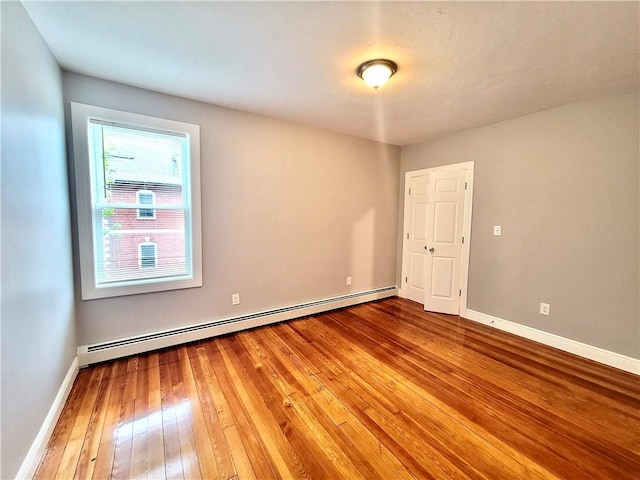 unfurnished room featuring hardwood / wood-style floors, a baseboard heating unit, and baseboards