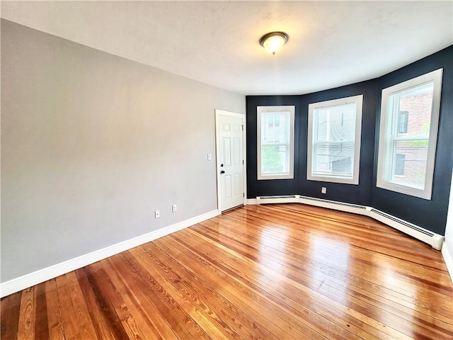 empty room with light wood-style flooring, baseboards, plenty of natural light, and a baseboard heating unit