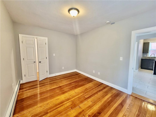 empty room with a baseboard heating unit, light wood-style floors, baseboards, and a sink