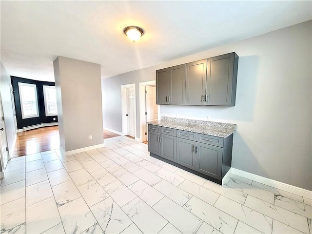 kitchen featuring baseboard heating, light marble finish floors, baseboards, and gray cabinets