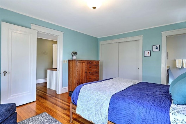 bedroom featuring wood finished floors, a closet, baseboards, and ornamental molding