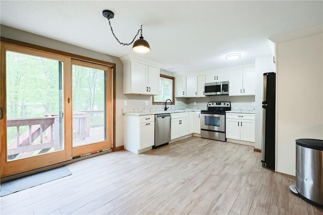 274 Courthouse Ln, Burrillville, RI 02859 - kitchen with stainless steel appliances, white cabinetry, light wood-style floors, a sink, and pendant lighting