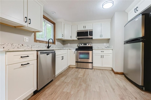 274 Courthouse Ln, Burrillville, RI 02859 - kitchen with stainless steel appliances, a sink, light wood-style floors, white cabinets, and a textured ceiling