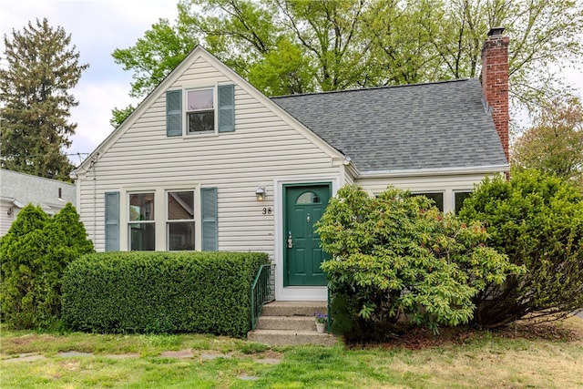 view of front of house with roof with shingles, a chimney, and a front yard
