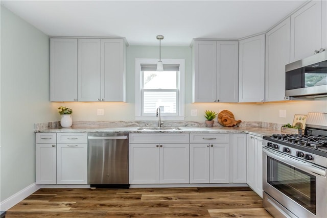 kitchen with appliances with stainless steel finishes, a sink, light stone countertops, wood finished floors, and hanging light fixtures