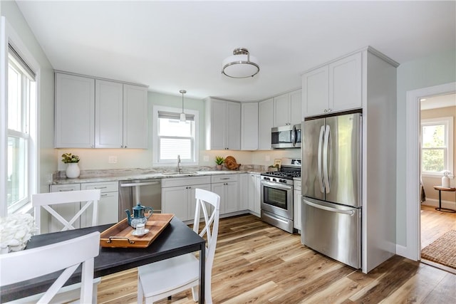 kitchen with stainless steel appliances, light wood-type flooring, a sink, light stone countertops, and baseboards