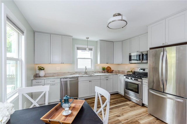 kitchen with appliances with stainless steel finishes, a sink, light wood finished floors, light stone counters, and decorative light fixtures