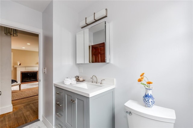 half bath featuring vanity, a brick fireplace, toilet, and baseboards