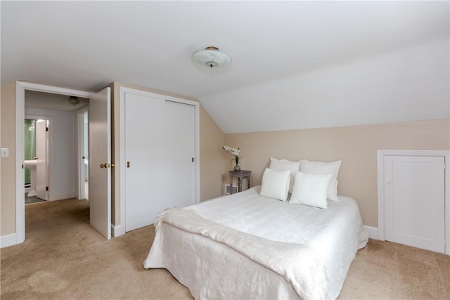 bedroom with light colored carpet, a closet, baseboards, and vaulted ceiling