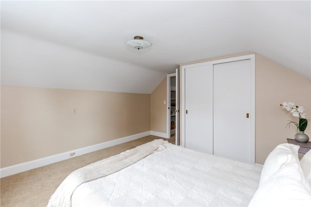 bedroom with carpet flooring, vaulted ceiling, baseboards, and a closet