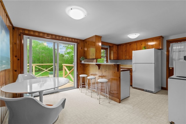 11 Cedar Ave, Middletown, RI 02842 - kitchen with freestanding refrigerator, wood walls, a breakfast bar area, a peninsula, and brown cabinets
