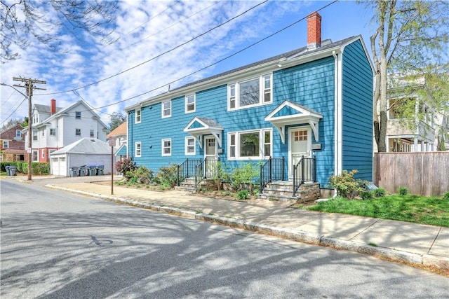 view of front facade featuring a chimney, an outdoor structure, fence, a residential view, and a detached garage