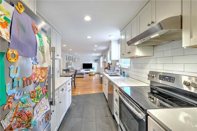 kitchen with stainless steel appliances, under cabinet range hood, open floor plan, a sink, and light countertops