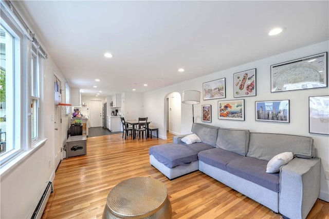 living area featuring arched walkways, light wood-style floors, baseboard heating, and recessed lighting
