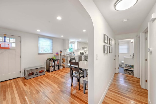 hallway featuring light wood finished floors, a sink, baseboards, arched walkways, and recessed lighting