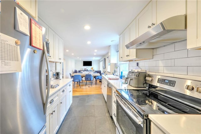 kitchen featuring stainless steel appliances, under cabinet range hood, a sink, open floor plan, and white cabinetry