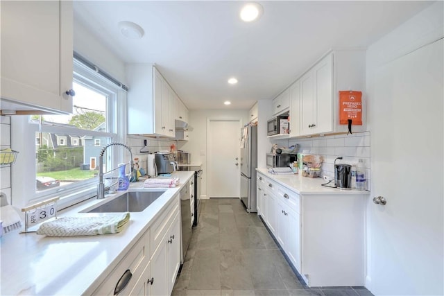 kitchen with a sink, stainless steel appliances, white cabinets, decorative backsplash, and light countertops