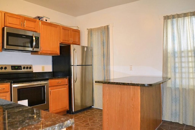 kitchen with appliances with stainless steel finishes, dark stone counters, and brown cabinets