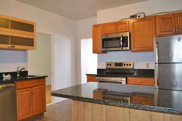 kitchen featuring appliances with stainless steel finishes, a sink, dark stone counters, and brown cabinets