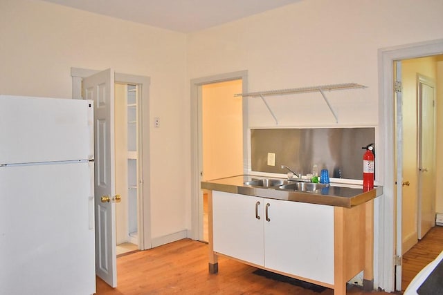 kitchen featuring freestanding refrigerator, a sink, light wood-style flooring, and white cabinetry