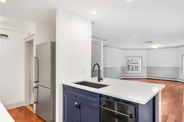 kitchen featuring freestanding refrigerator, a sink, a peninsula, blue cabinetry, and light countertops