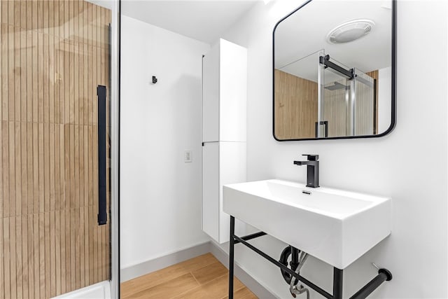 bathroom featuring wood finished floors, a shower with shower door, and baseboards