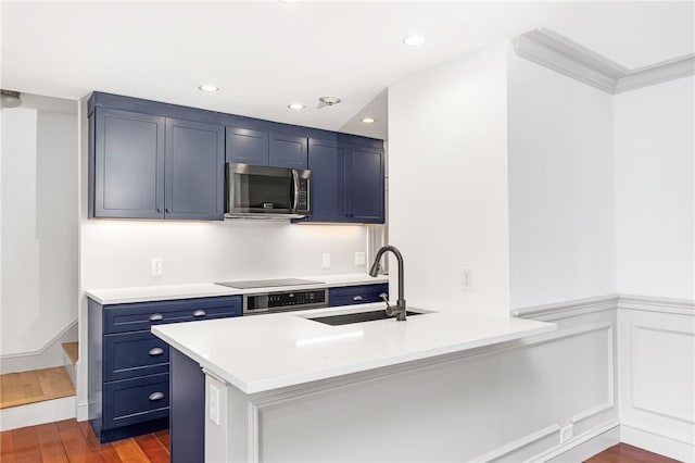 kitchen featuring stainless steel microwave, blue cabinets, a sink, dark wood-style floors, and a peninsula