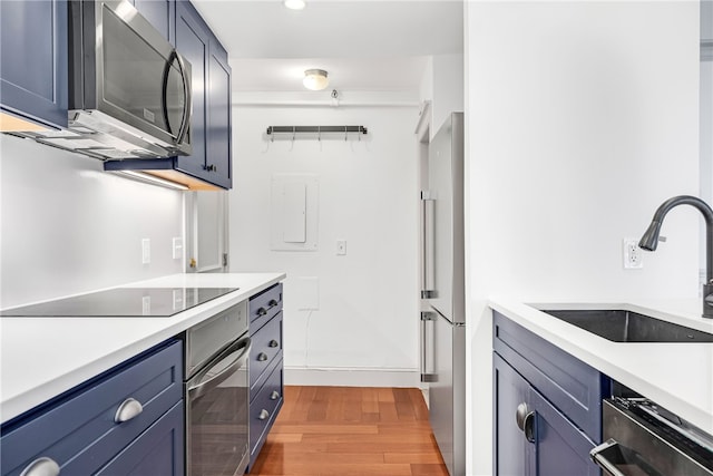 kitchen featuring appliances with stainless steel finishes, a sink, light wood-style flooring, light countertops, and blue cabinets