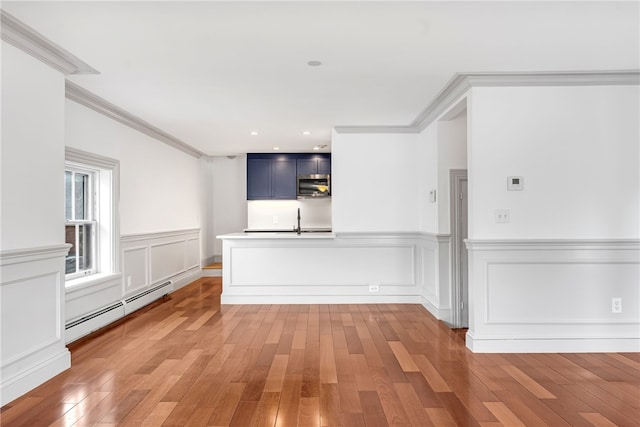 empty room with a baseboard radiator, a sink, light wood-style flooring, crown molding, and a wainscoted wall