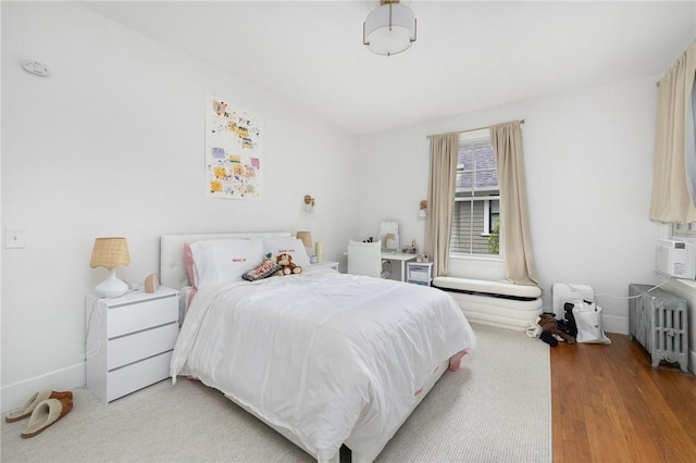 bedroom with radiator, wood finished floors, and baseboards
