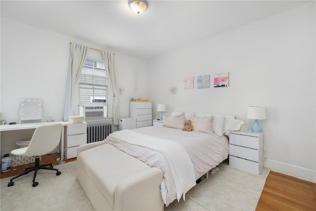 bedroom featuring radiator, wood finished floors, baseboards, a desk, and cooling unit
