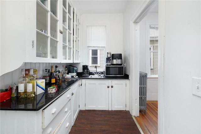 kitchen with dark wood-style floors, dark countertops, a sink, stainless steel microwave, and white cabinets