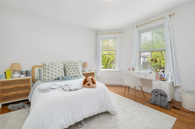 bedroom with multiple windows, wood finished floors, and baseboards