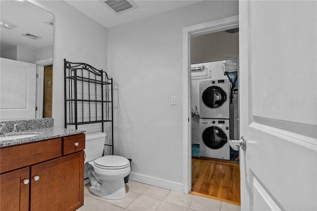 bathroom featuring stacked washing machine and dryer, tile patterned flooring, toilet, vanity, and baseboards