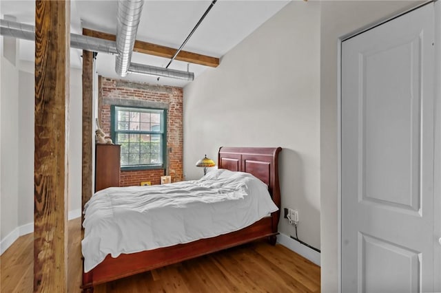 bedroom featuring wood finished floors, brick wall, and baseboards