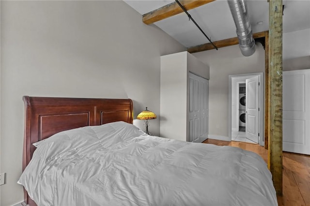 bedroom with stacked washer and clothes dryer, high vaulted ceiling, wood finished floors, baseboards, and beamed ceiling