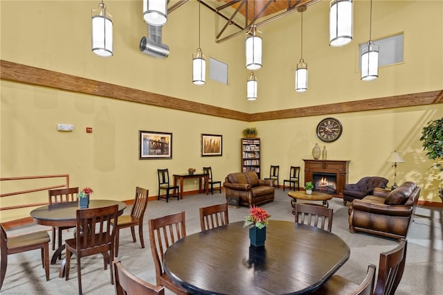 dining room featuring a towering ceiling, a lit fireplace, and baseboards